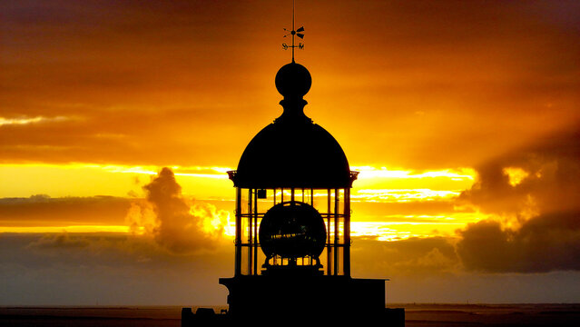 Aerial view of the lantern room of the Pointe Saint-Mathieu lighthouse silhouetted against a vibrant golden sunset sky in Plougonvelin, Brittany, France.