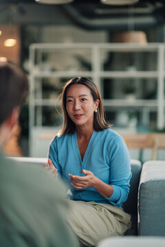 Asian businesswoman discussing and gesturing, participating in a professional meeting, sharing ideas in a modern office lounge