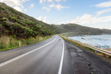 Fototapeta premium Deserted stretch of a coast road on a clear autumn day. A thin mist coming form the ocean hang over the road. Great Ocean Road, VIC, Australia.