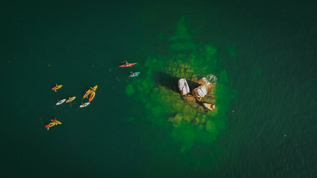 Aerial view of kayakers paddling near the rocky outcrop of Pointe du Cosmeur in the clear green waters of Carantec, Bretagne, France.