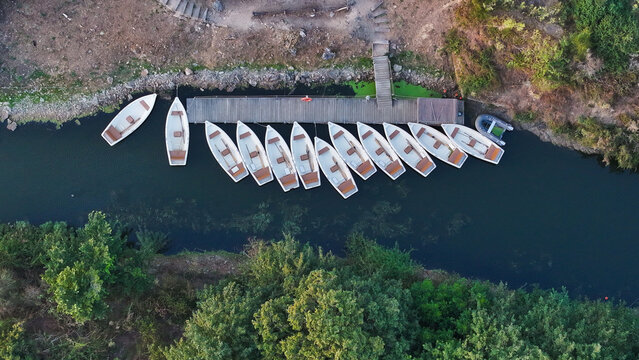 Aerial view of Domaine de Suscinio showing a row of small wooden boats moored at a wooden pier in a calm canal surrounded by lush green trees in Sarzeau, Bretagne, France.