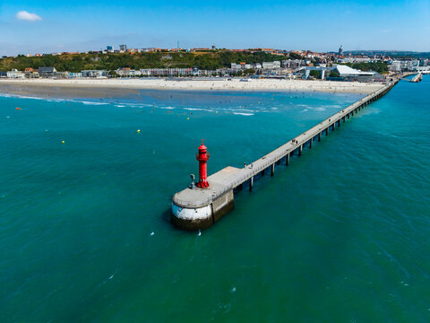 Aerial view of the red lighthouse at the end of the pier at the Port de Boulogne-sur-Mer with the sandy beach and city skyline in Boulogne-sur-Mer, Hauts-de-France, France.