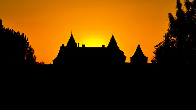 Aerial view of the silhouette of the historic Chateau de Suscinio at sunset, with dark castle towers and turrets set against a vibrant orange sky in Sarzeau, Bretagne, France.