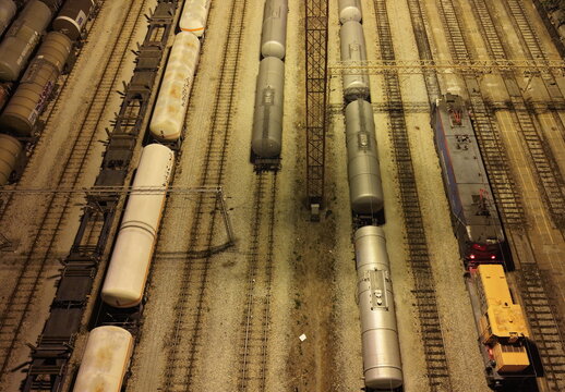 Aerial view of a freight train yard at night featuring rows of cylindrical tank cars and a locomotive parked on illuminated tracks in Omoljica, Vojvodina, Serbia.