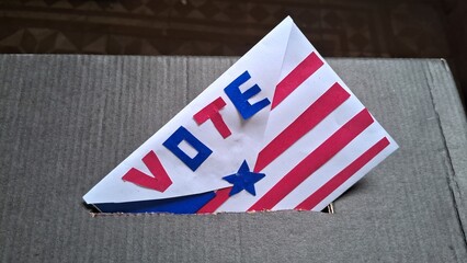 Obraz premium Decorative patriotic ballot envelope inserted into a simple cardboard voting box