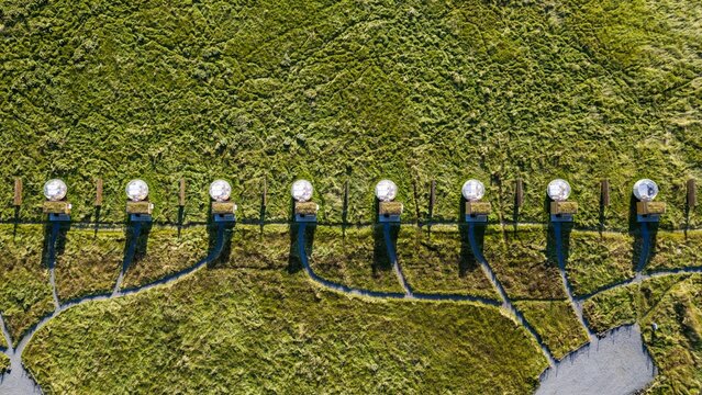 Aerial view of bubble hotel pods arranged in a row within a vast green field in Hella, Rangarthing ytra, Iceland.