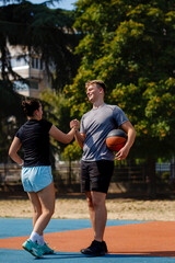Fototapeta premium Basketball players enjoying a friendly moment while practicing on an outdoor court in bright sunlight, surrounded by trees and urban scenery