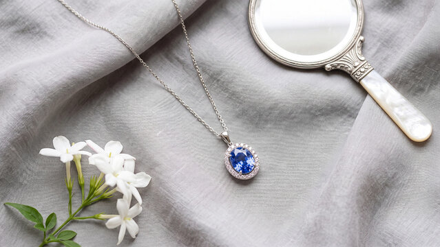Saphire pendant necklace on grey linen beside white blossoms and a mirror