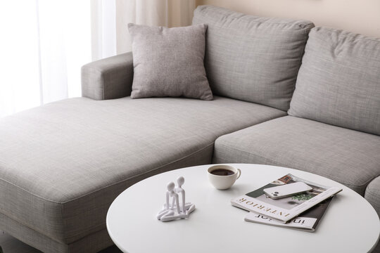 Modern gray sectional sofa with chaise lounge in a minimalist living room interior, coffee table with decor and smartphone