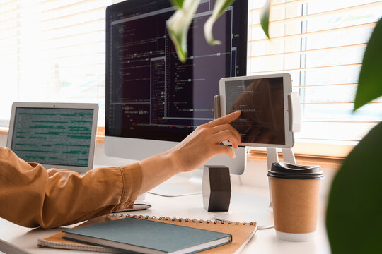 Programmers hand touching a tablet screen with code, multiple monitors displaying software development, modern office workspace