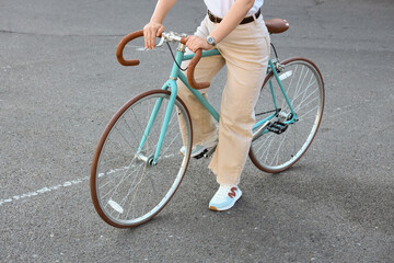 Fototapeta premium Person riding a vintage turquoise bicycle with brown handlebars and seat on an asphalt road, active lifestyle and urban transport