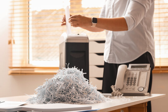 Person shredding confidential documents with a paper shredder data protection and privacy in an office environment