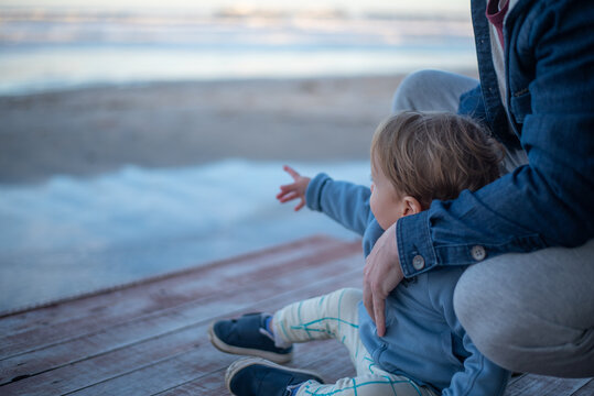 A 20-month-old toddler boy standing on the beach with his father and pointing at something in the distance