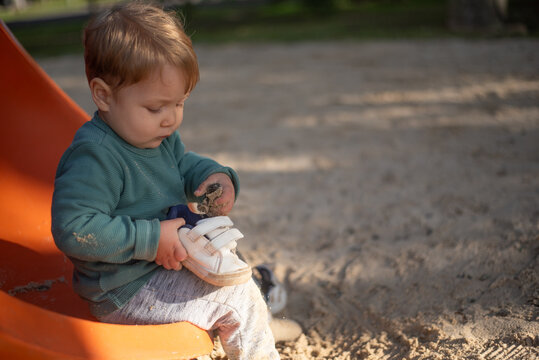 A 20-month-old toddler boy playfully putting sand inside his own sneaker