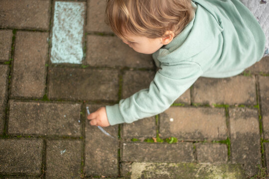 A 23-month-old left-handed toddler boy lying on the ground and drawing with chalk