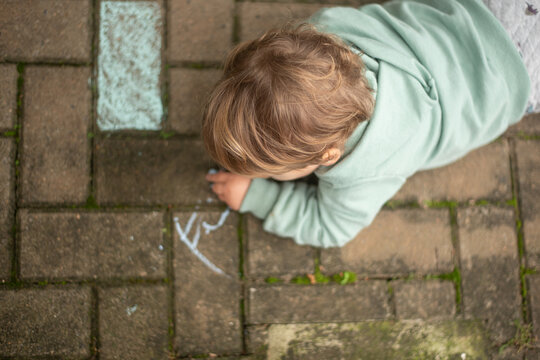 A 23-month-old left-handed toddler boy lying on the ground and drawing with chalk