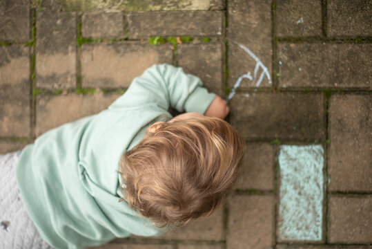 A 23-month-old left-handed toddler boy lying on the ground and drawing with chalk