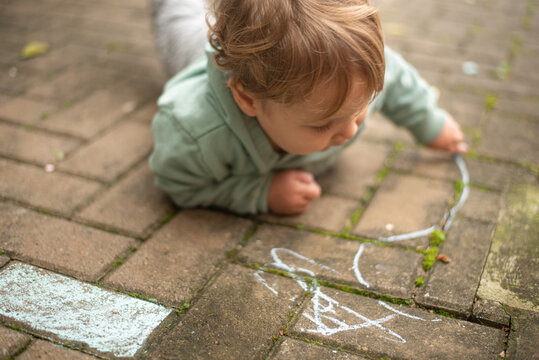 A 23-month-old left-handed toddler boy lying on the ground and drawing with chalk