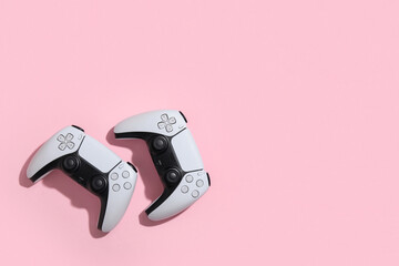 Two modern white video game controllers with black accents on a solid pink background, gaming and entertainment, this image gaming entertainment and technology concepts © Pixel-Shot