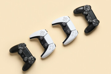 Four modern video game controllers, two black and two white, arranged diagonally on a light beige background © Pixel-Shot
