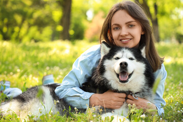Happy young woman embracing her siberian husky dog while relaxing in a sunny green park, the woman and dog are smiling, showing a strong bond and companionship © Pixel-Shot