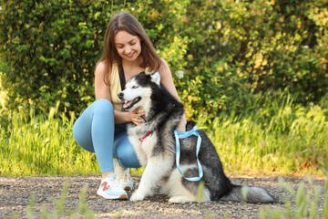 Young woman crouching and petting her happy siberian husky dog outdoors in a park setting, the happy dog has blue eyes and a black and white coat, sitting patiently on a gravel path © Pixel-Shot