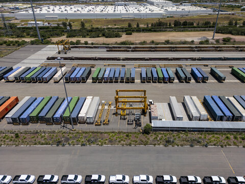 Aerial view of a logistic center with rows of colorful shipping containers, a gantry crane, and parked white pickup trucks in San Luis Potosi, San Luis Potosi, Mexico.