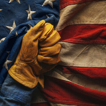 Hand in worn work glove holding the American flag. Symbolic of hardworking blue collar workers, USA manufacturing, pride in products Made in United States of America, or to celebrate US Labor Day.