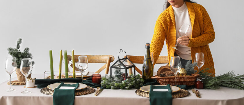 Woman setting a festive christmas or new year's eve dinner table with elegant decor and wine glasses