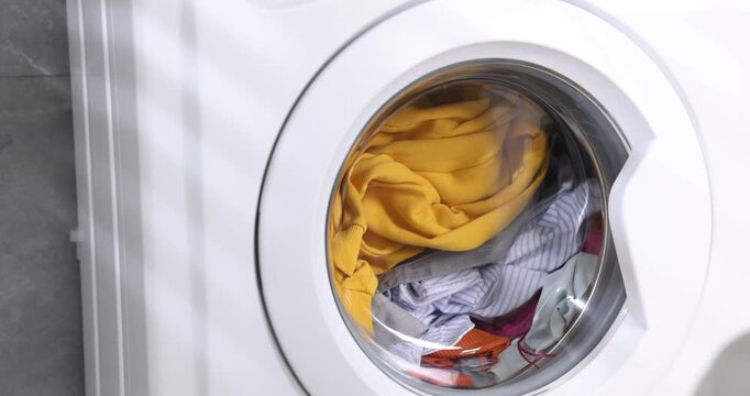 Woman loading washing machine and closing door, closeup. Laundry day