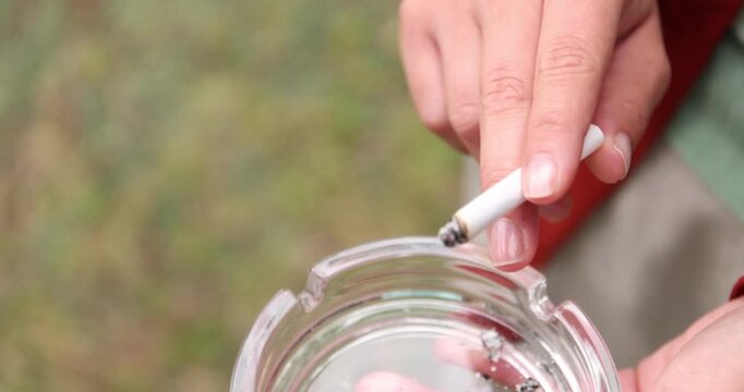 Woman flicking ash from cigarette into ashtray outdoors, closeup. Camera moving in