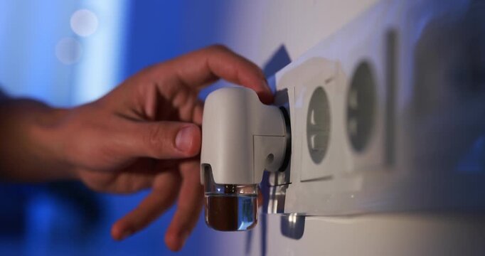 Man plugging in electric mosquito repeller with liquid refill at home at night, closeup