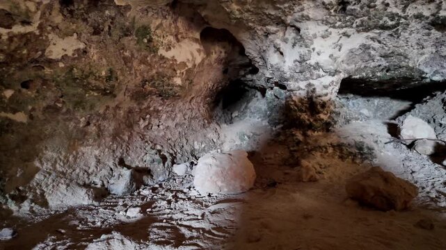 Dusty cave floor with scattered stones and moss. Water trickles through rocky crevices. Wet earth shows signs of ancient seepage. Cave walls reveal weathered textures. Ideal for exploratory