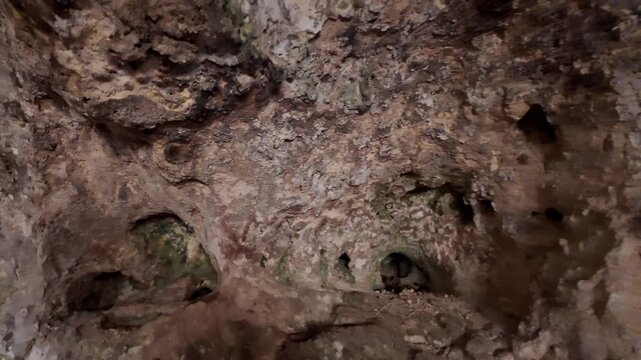 Dark cave walls show rugged textures and patches of green moss. Fragments of ancient rock formations hint at deep history. Natural light barely reaches this secluded underground chamber