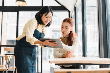 Fototapeta premium Asian waitress taking customer order on digital tablet at coffee shop table