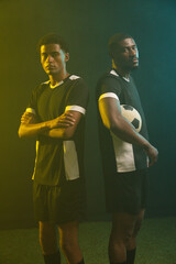 Fototapeta premium African male teammates posing back-to-back on turf, wearing black-white kits, holding soccer ball
