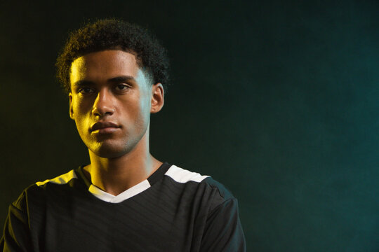 African American man posing in studio, charcoal jersey white V-neck lit by teal-yellow rim lights