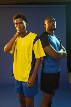 Two male African American athletes posing in studio with blue backdrop wearing yellow-blue jersey