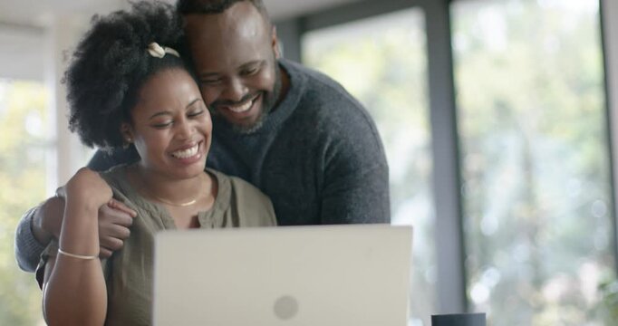 African couple sitting at table man coming leaning over shoulder woman typing cheering on laptop