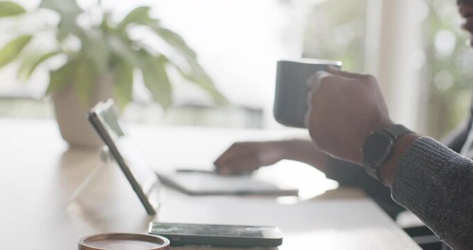 Right hand is reaching for blue mug to sip while left is tapping tablet near window