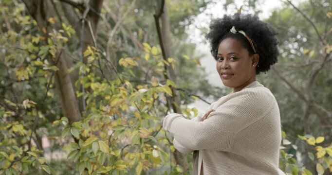 African American woman noticing camera folding arms, turning, laughing among trees wearing headband