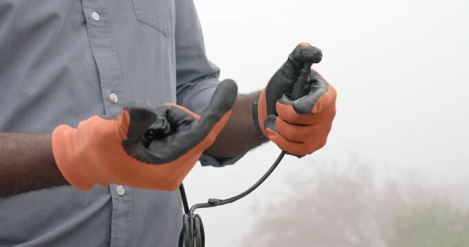 Adult African man wearing orange gloves holding connectors and inspecting showing latch in fog