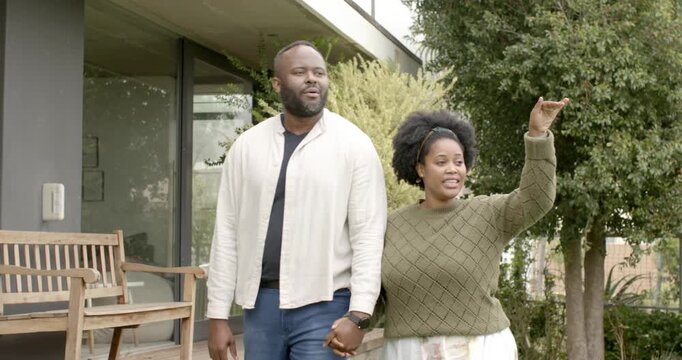 African American couple stepping off porch, walking holding hands, woman pointing out garden