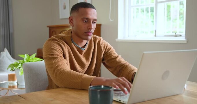 African American man late 20s starting work at home, typing on laptop with coffee mug, smiling