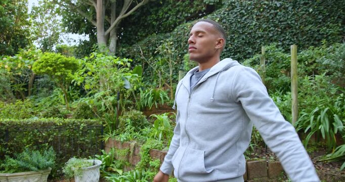 African man pressing palms, breathing and stretching for calm in garden wearing hoodie and watch
