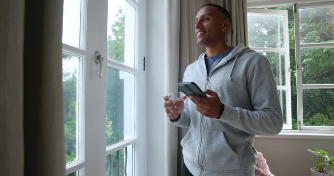 African American man by home window reading phone tucking into pocket taking pill drinking