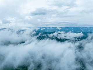 Naklejka premium A high-angle view of mountain ranges partially obscured by thick clouds and mist, showcasing a serene natural landscape.