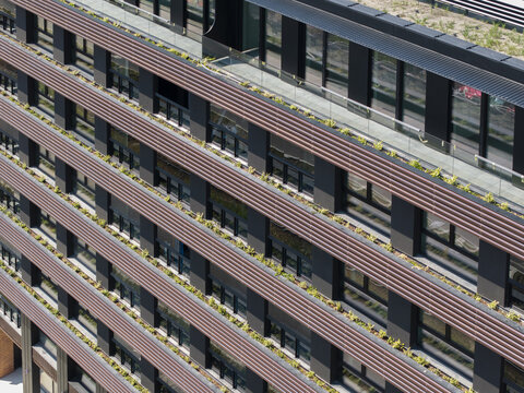 Aerial view of modern building facade with horizontal brown louvers and balcony greenery in Poland.