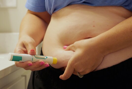 Woman giving herself auto-injector injection in abdomen for biologic allergy therapy, GLP-1 weight loss medication, or chronic medical treatment
