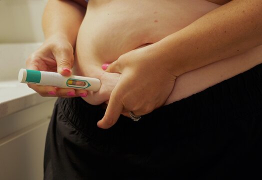 Woman giving herself auto-injector injection in abdomen for biologic allergy therapy, GLP-1 weight loss medication, or chronic medical treatment